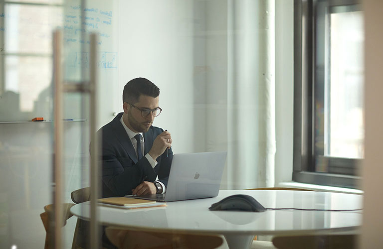 Chris Fundora wearing a dark suit and tie, looking intently at his laptop's screen.