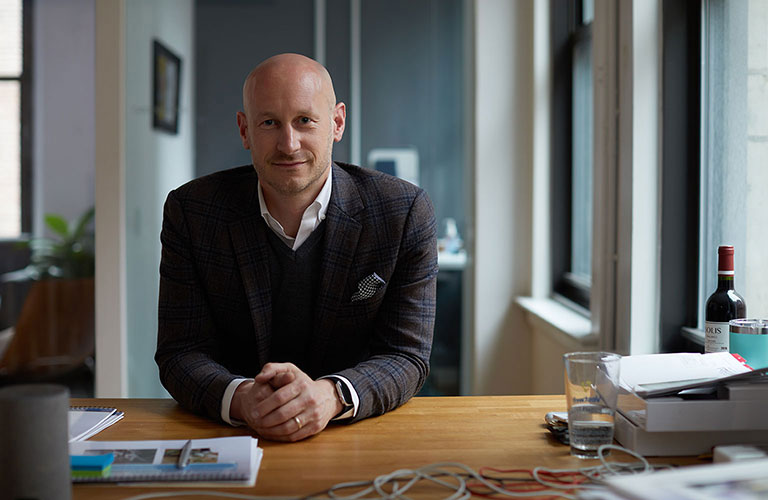 Aaron Schumm, CEO & Founder of Vestwell, wearing a dark wool sport coat, his hands folded in front of him, smiling warmly at the camera.