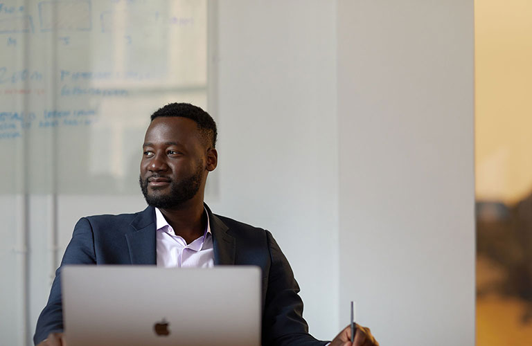 Bill Simonet wearing a dark grey sport coat and a contented look on his face, sitting at his computer.